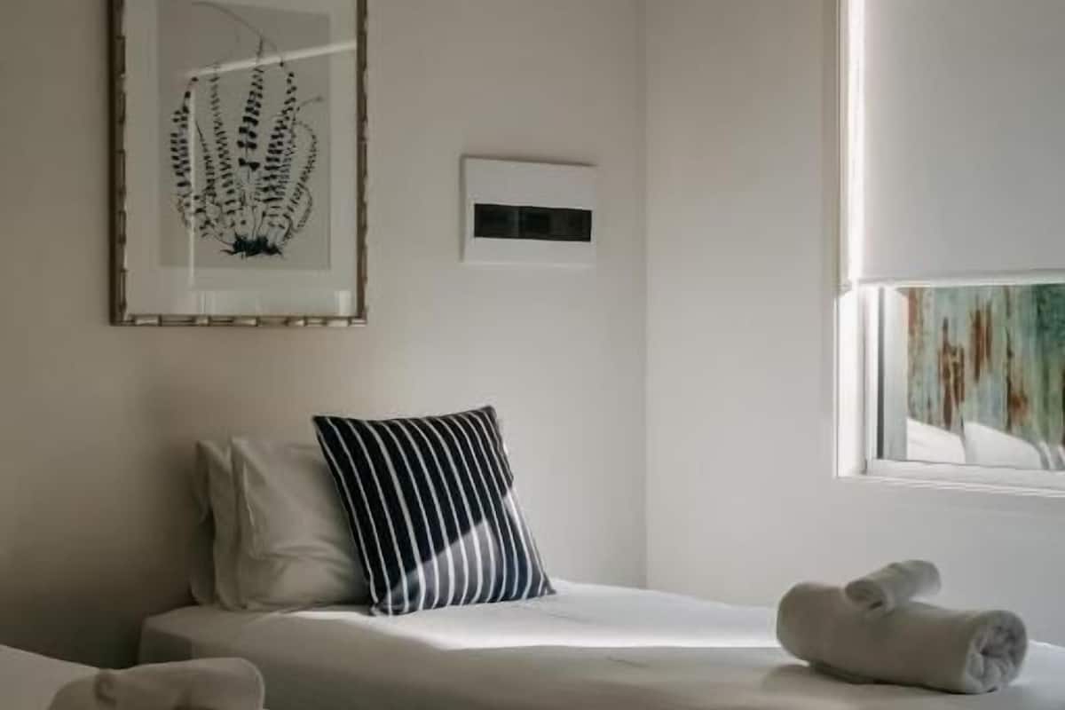 Ett hotellrum med två sängar, ett fönster med persienner, ett inramat konstverk på väggen och en kudde på en av sängarna.