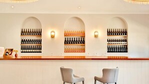 A bar area with three arched shelves displaying wine bottles, two bar stools, and wall-mounted lighting.