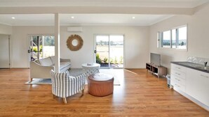 A spacious living area with a sofa, ottoman, and a round table. There is a large window providing a view of the outdoors.