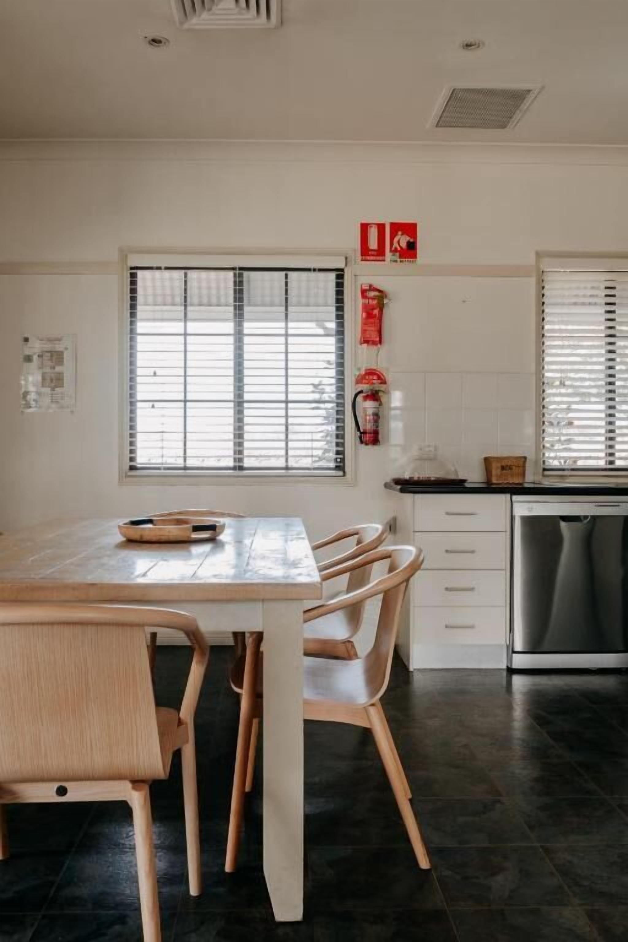 A modern kitchen with a dining table, chairs, a dishwasher, and a window with blinds.