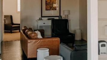 A living room with a brown leather sofa, a grey armchair, and a white coffee table. There is a framed picture on the wall and a small white side table.