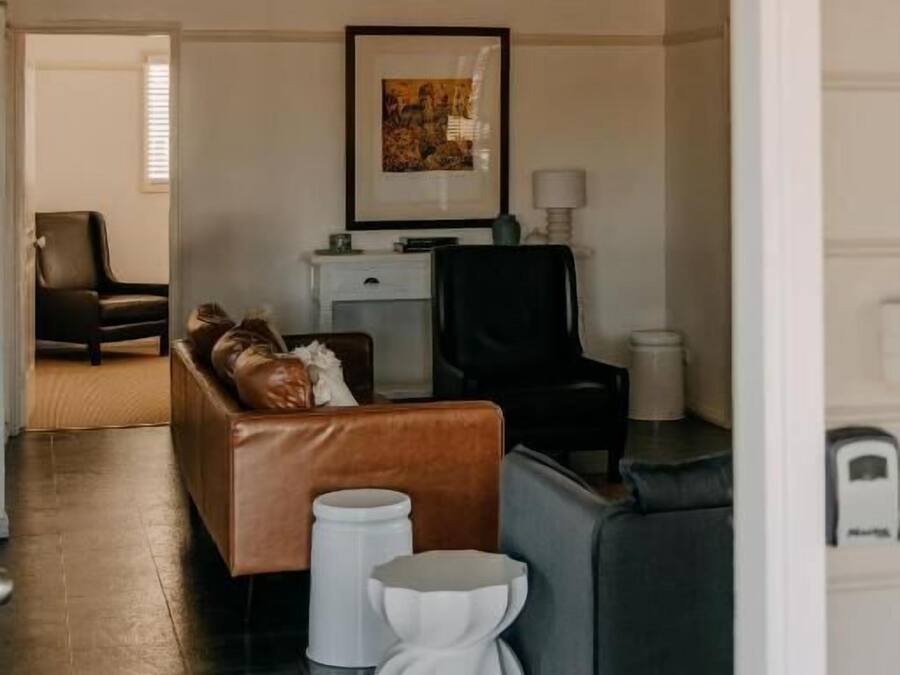A living room with a brown leather sofa, a grey armchair, and a white coffee table. There is a framed picture on the wall and a small white side table.