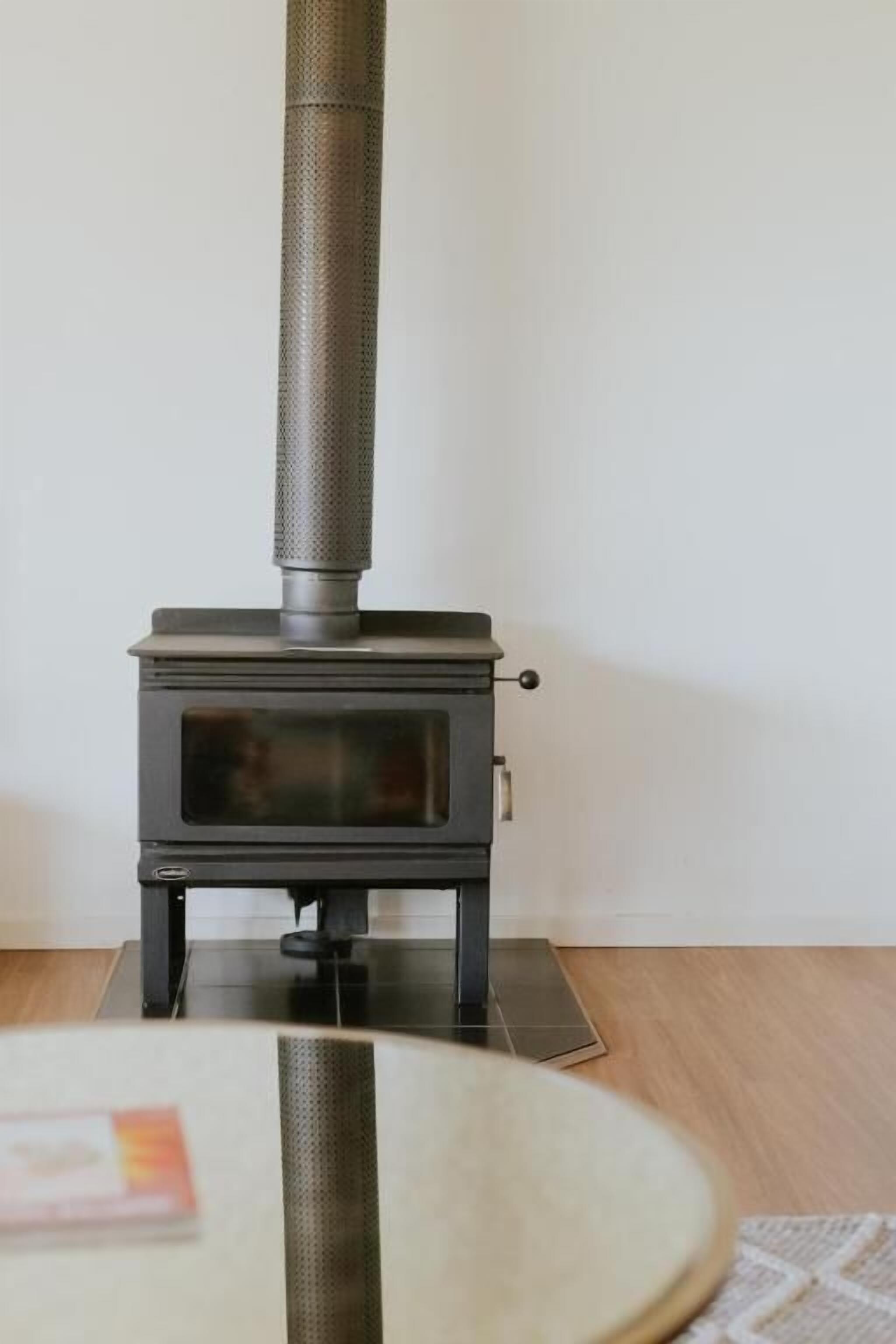 A wood-burning stove in a room with a tiled floor and a round table in the foreground.