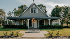A two-story house with a gabled roof, a porch with white columns, and a small garden area in front.