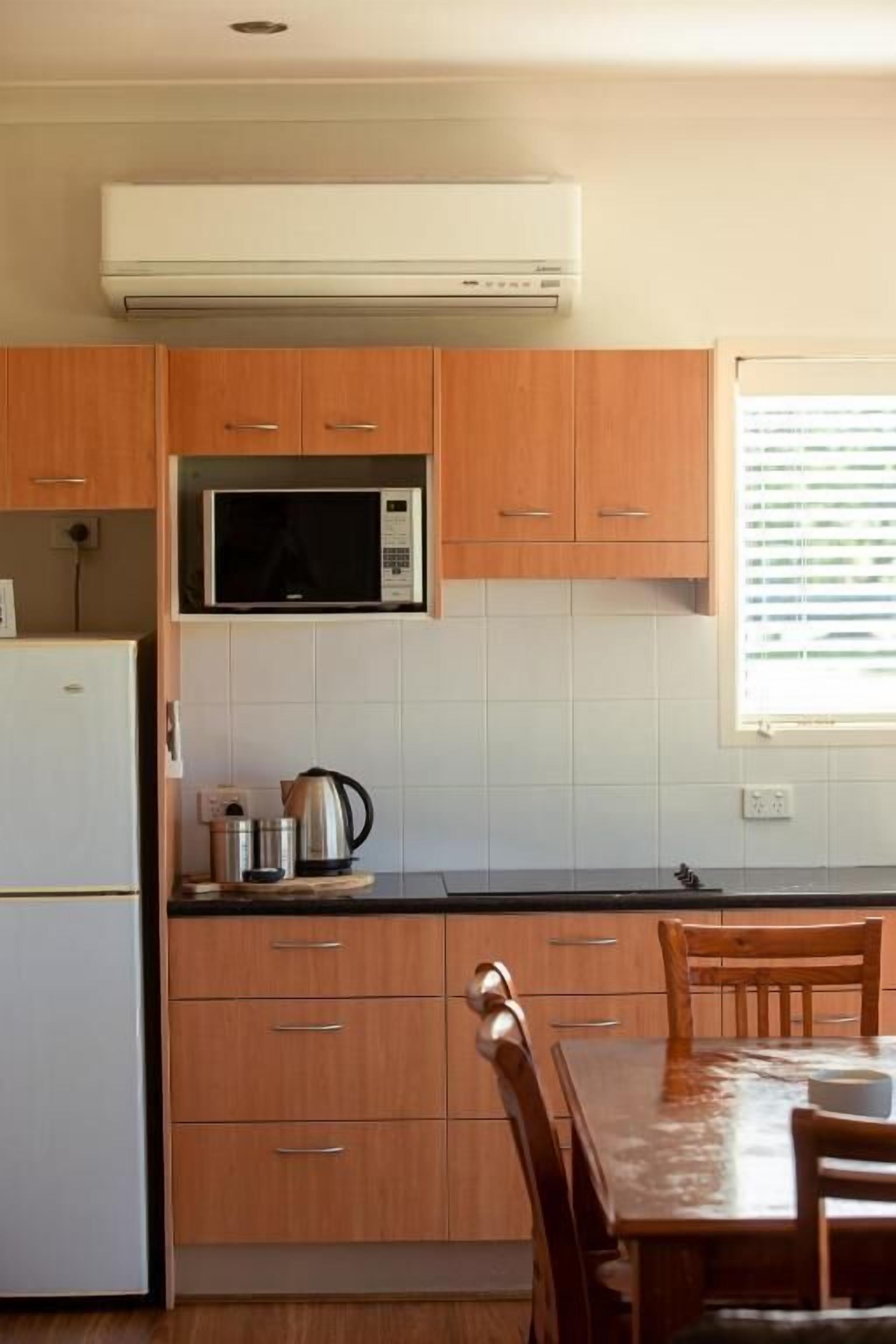 Una cocina con armarios de madera, un microondas, un refrigerador y una mesa de comedor con sillas.