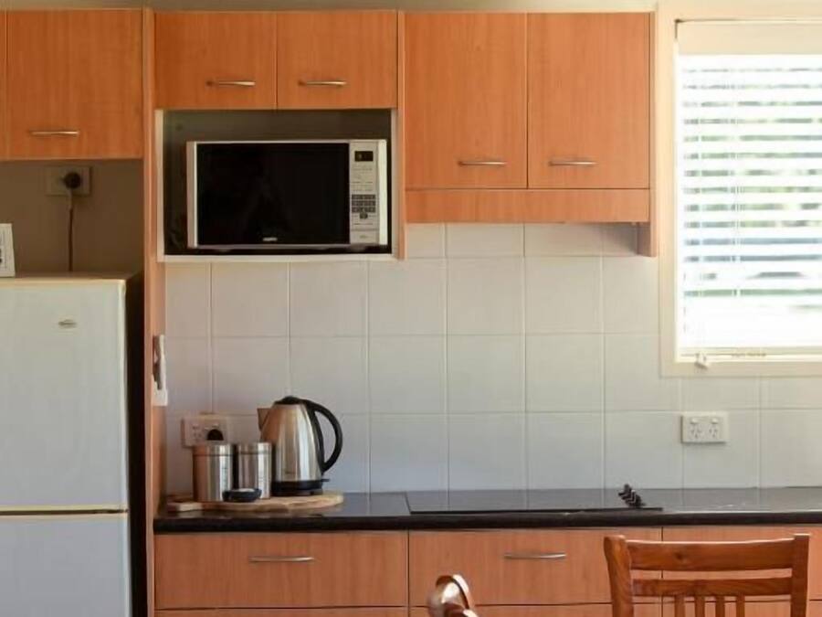 A kitchen with wooden cabinets, a microwave, a refrigerator, and a dining table with chairs.