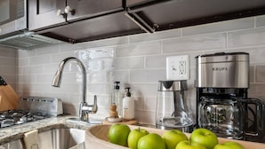 Una cocina moderna con estufa de acero inoxidable, horno empotrado, cafetera y un tazón de manzanas verdes sobre la encimera.