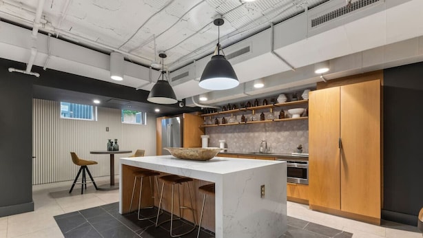 Una cocina moderna con una isla central, taburetes de bar, iluminación colgante y armarios de madera.