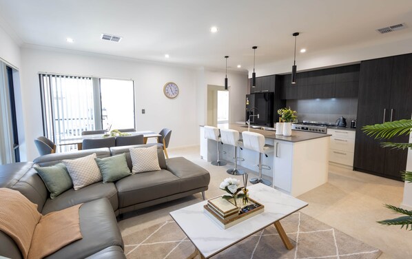 Un salon moderne avec un canapé, une table basse et un coin cuisine doté de meubles sombres et d’une cuisinière.