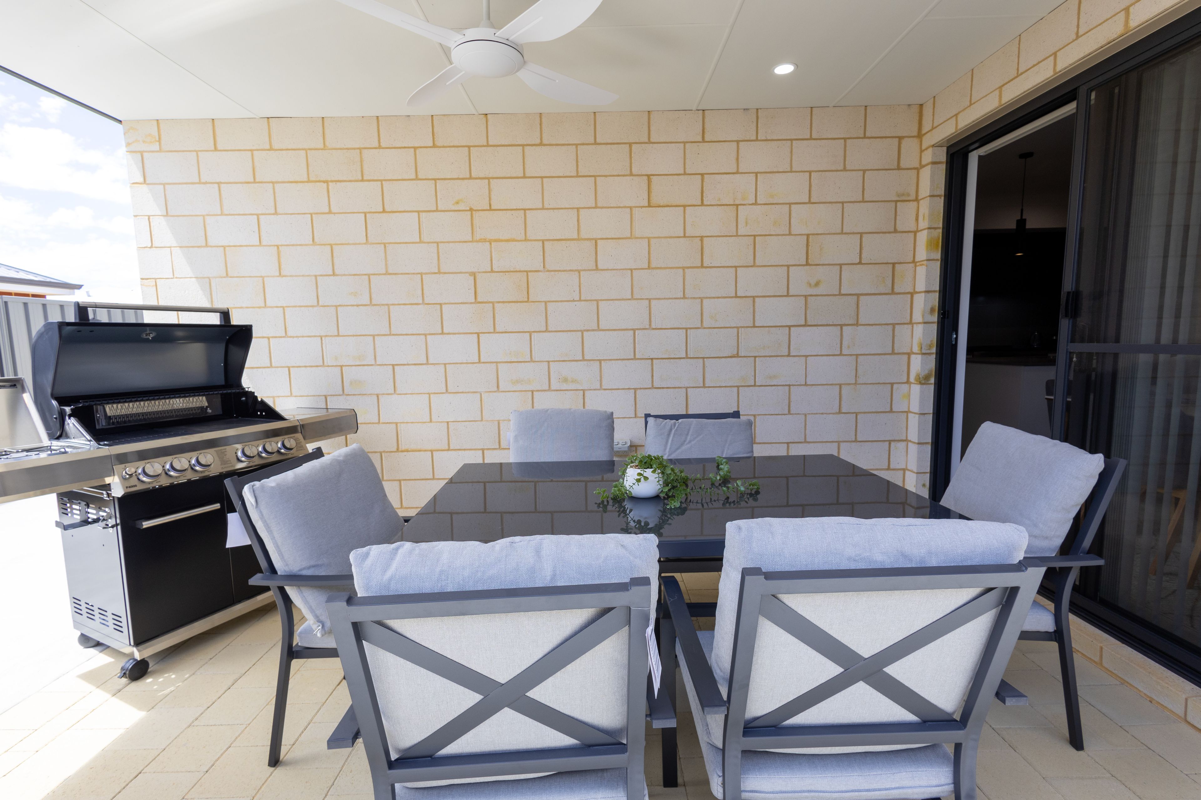 Un patio con pared de ladrillo, una parrilla y una mesa con sillas.