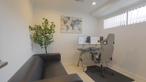 A modern office space with a black leather couch, a desk with two monitors, a Typhoon gaming chair, a world map on the wall, and a potted plant.
