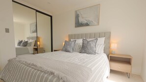 A bedroom with a large bed, a nightstand, a mirror, and a painting on the wall.