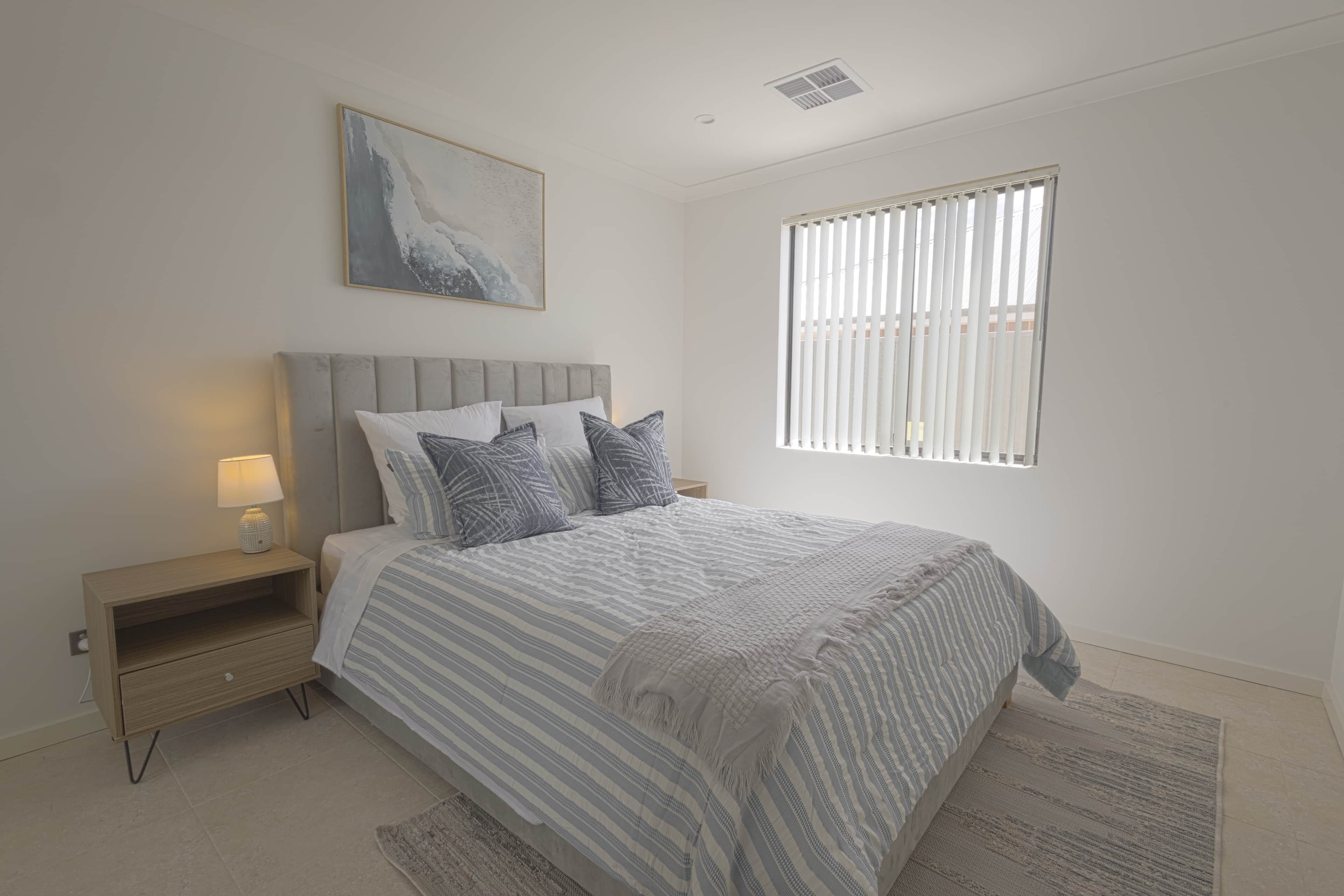 A bedroom with a bed, nightstand, lamp, and a window with blinds.