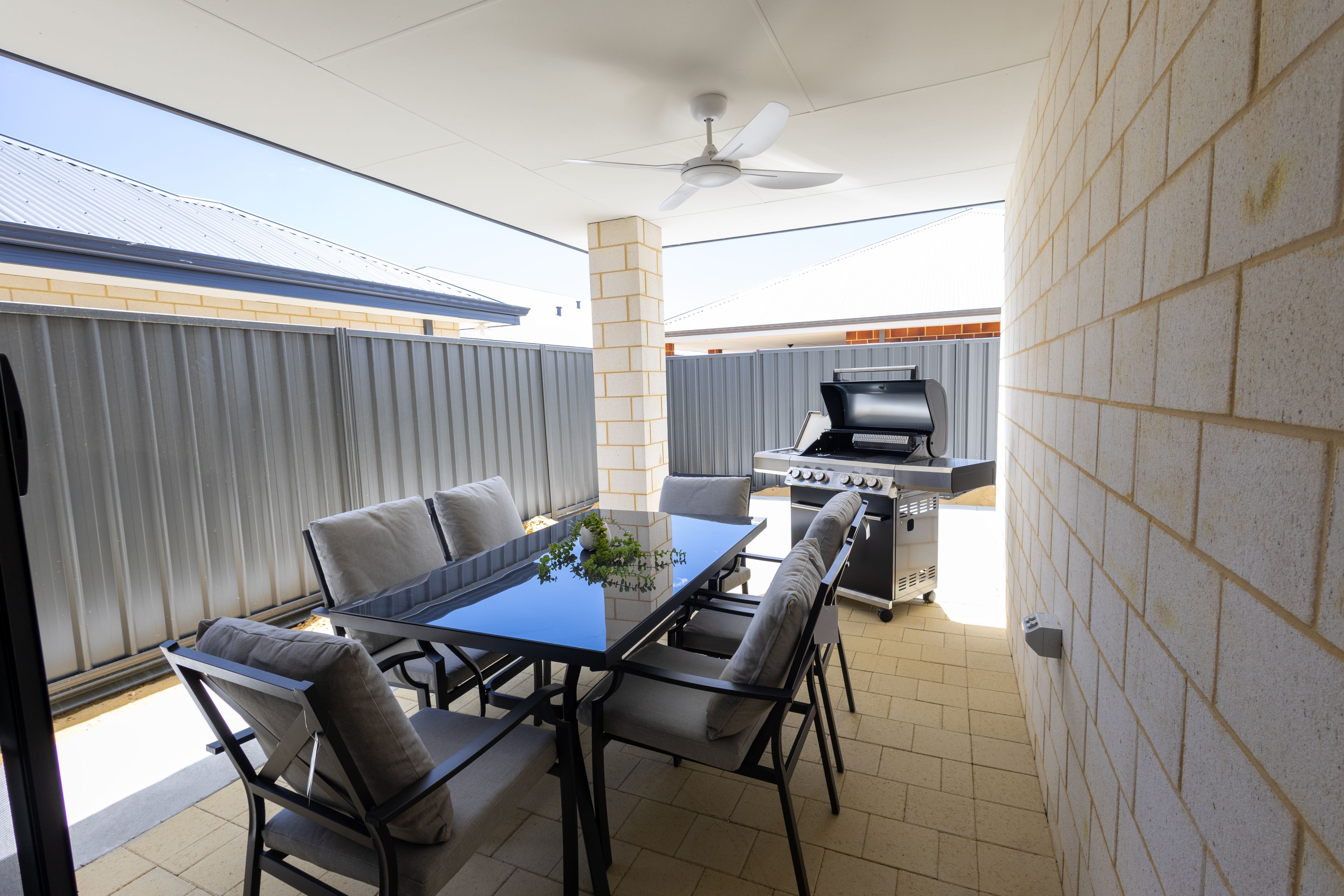 An outdoor patio with a table and chairs, a ceiling fan, and a barbecue grill.