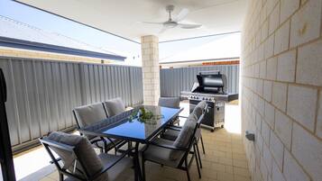 An outdoor patio with a table and chairs, a ceiling fan, and a barbecue grill.