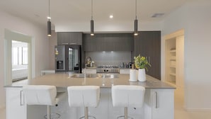 A modern kitchen with a central island, three pendant lights, and white bar stools.