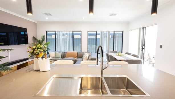 A modern kitchen with a stainless steel sink, a dining area with a table and chairs, and a living area with a sofa and a TV.