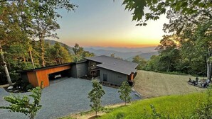 Een modern huis met een ruime garage en een overdekt terras, omgeven door een weelderig landschap en op de achtergrond bergen.