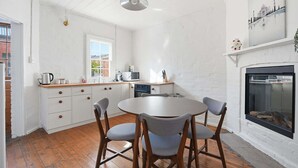 A kitchen with white cabinets, a round table, and four chairs. There is a window, a microwave, and a kettle on the counter.