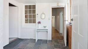 A hallway with white walls, a stone-tiled floor, a white door, and a window with a white frame.