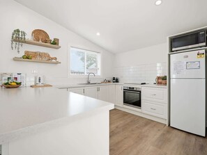 A modern kitchen with white cabinetry, a built-in oven, a refrigerator, and a window with blinds. - William Cottage • Walkable CBD Base • Bathurst (Bathurst)