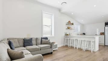 Un salon moderne avec un canapé gris et un coin cuisine doté d’un bar blanc et de tabourets.