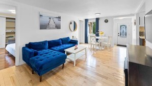 A modern living room with a blue sofa, a white coffee table, and a dining area with a white table and chairs. - Cozy Family Retreat Minutes From Falls  (Niagara Falls)