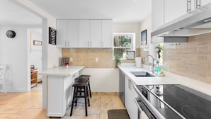 A modern kitchen with white cabinets, a black stove, and a window above the sink. - Cozy Family Retreat Minutes From Falls  (Niagara Falls)