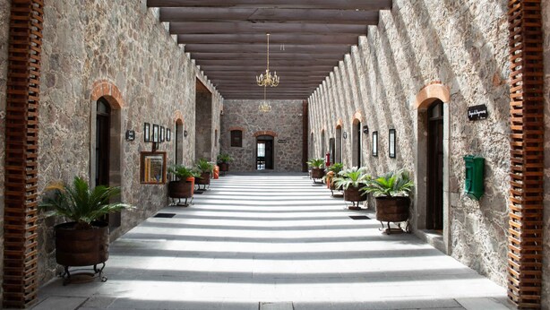 A corridor with stone walls, wooden beams, and potted plants. - Centro Vacacional La Trinidad (Santa Cruz Tlaxcala)