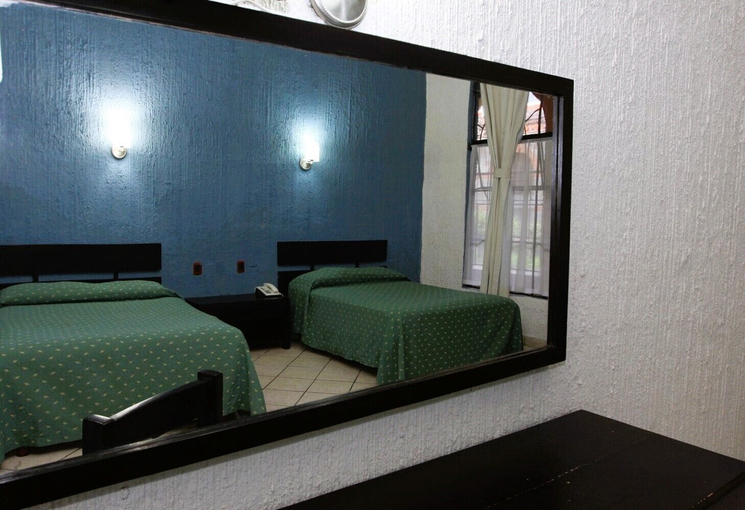 Habitación de hotel con dos camas individuales, una mesita de noche con teléfono y un espejo grande que refleja la habitación.