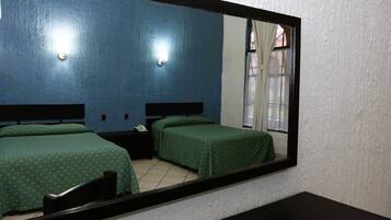 Habitación de hotel con dos camas individuales, una mesita de noche con teléfono y un espejo grande que refleja la habitación.