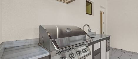 Eine Outdoor-Küche aus Edelstahl mit integriertem Grill, einer Spüle und einem Schrank.