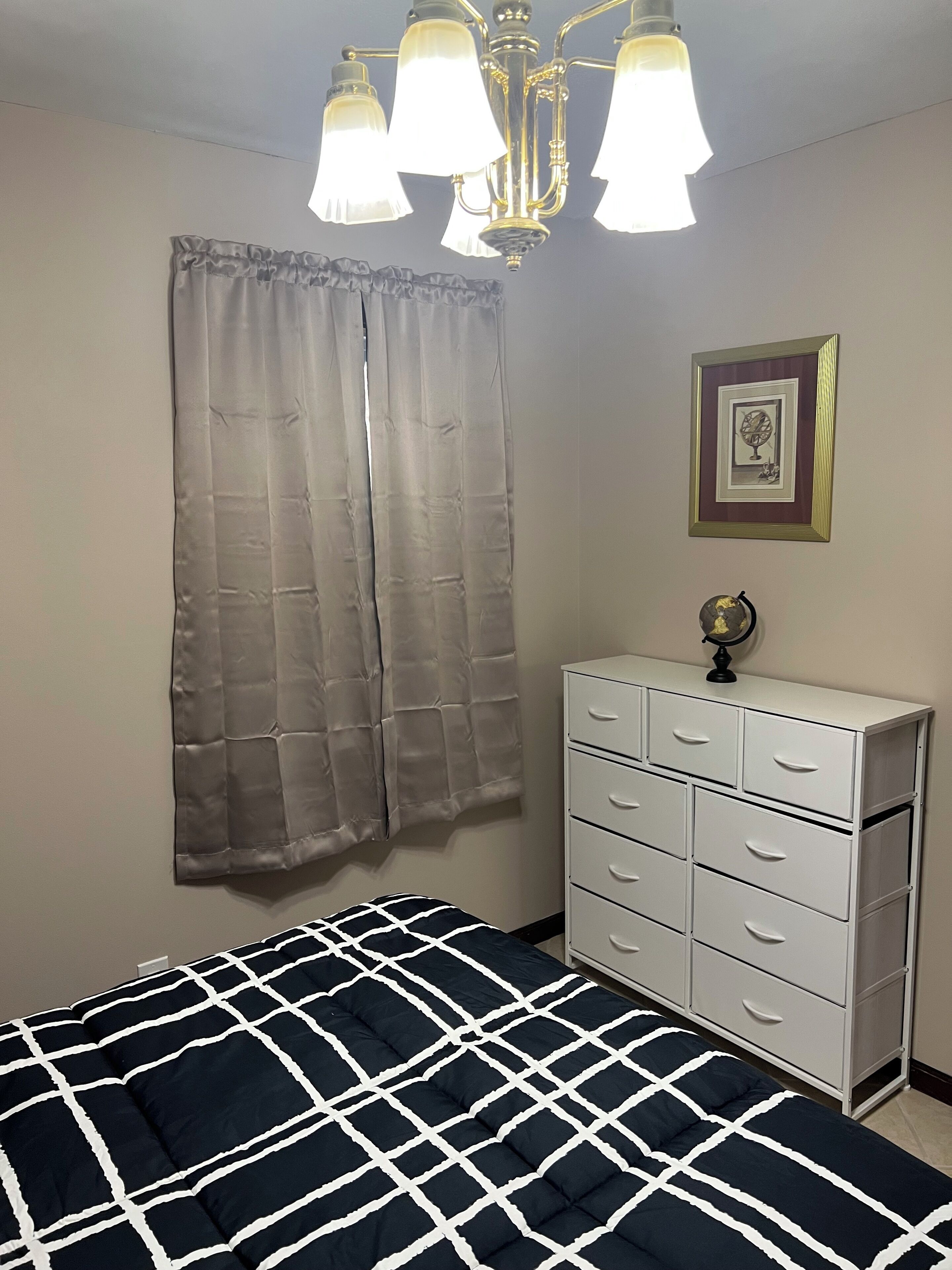 Une chambre à coucher avec un lit, une commode, un lustre et un tableau encadré accroché au mur.