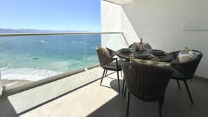 Ein Balkon mit Meerblick, einem Tisch mit Stühlen und einer Weinflasche.