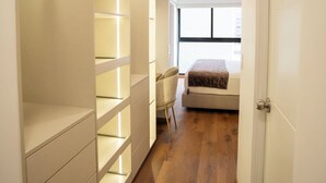 A narrow hallway with a built-in closet on the left, a bed with a headboard in the center, and a desk with a chair in the background. -  Miraflores Prime Apartment-3 blocks to Kennedy Park (Miraflores)
