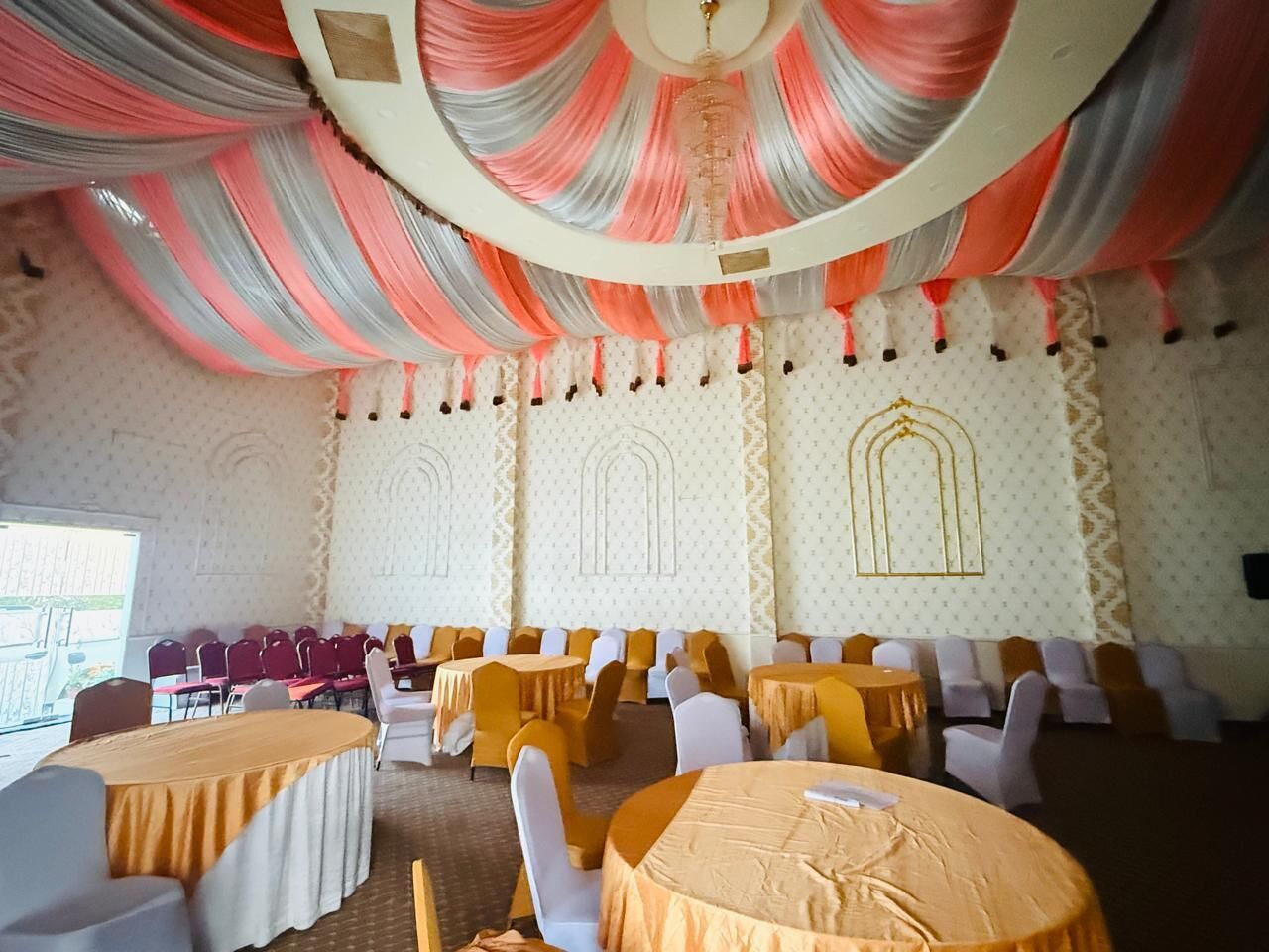 A banquet hall with round tables, chairs, and a patterned wall.