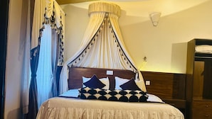 Una camera d'albergo con un letto, una testiera in legno, un comodino con un telecomando e un tavolino di servizio.