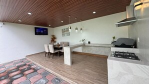 Una cocina moderna con estufa a gas integrada, una zona de comedor con banco y sillas, y un techo de madera con iluminación empotrada.