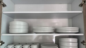 Un armario blanco con estantes que contienen platos y tazas blancas.