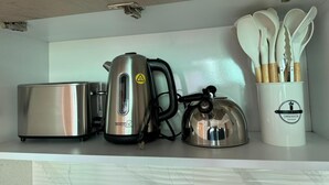 Una encimera de cocina con un tostador, una tetera y una taza con utensilios.