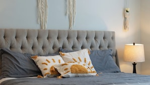 A bed with a tufted headboard, two pillows with a sun design, a blue bedspread, and a bedside lamp. - Boho 3BR Alhambra, Sleeps 8, Pet OK, DTLA/Disney/Universal/World Cup/Olympics (Alhambra)