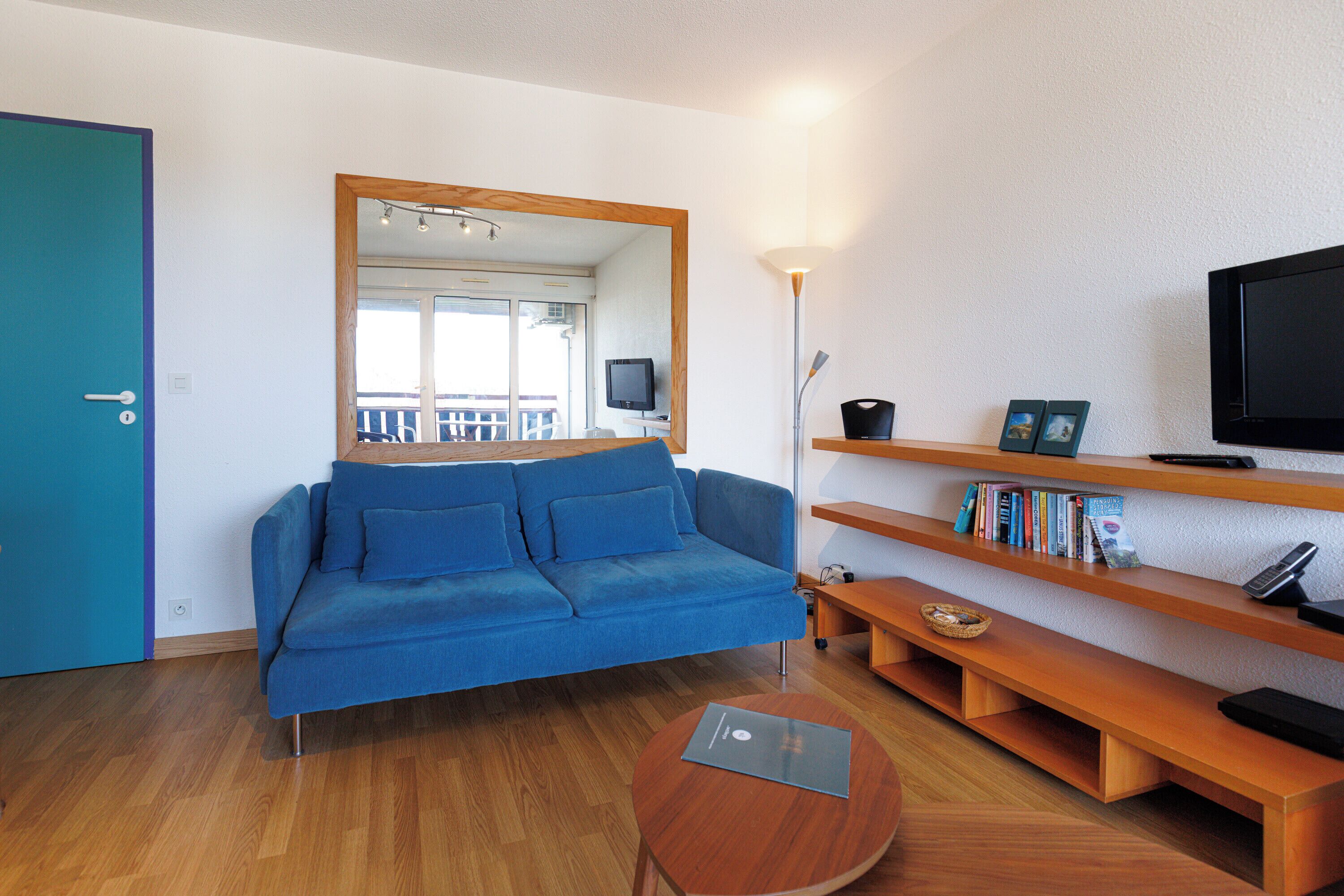 A modern living room with a blue sofa, wooden shelves, a TV, and a laptop on a round table.