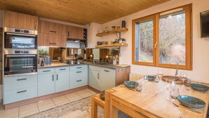 A modern kitchen with wooden cabinets, a built-in oven, and a dining area with a table set for four. - Appartement Rocca - Welkeys (Saint-Gervais-les-Bains)