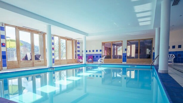 An indoor swimming pool with clear glass walls, wooden doors, and blue-tiled walls. - Appartement Rocca - Welkeys (Saint-Gervais-les-Bains)