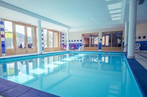 An indoor swimming pool with clear glass walls, wooden doors, and blue-tiled walls. - Appartement Rocca - Welkeys (Saint-Gervais-les-Bains)