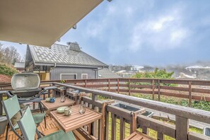 Une terrasse extérieure avec un barbecue, des tables et des chaises en bois, donnant sur un paysage enneigé.