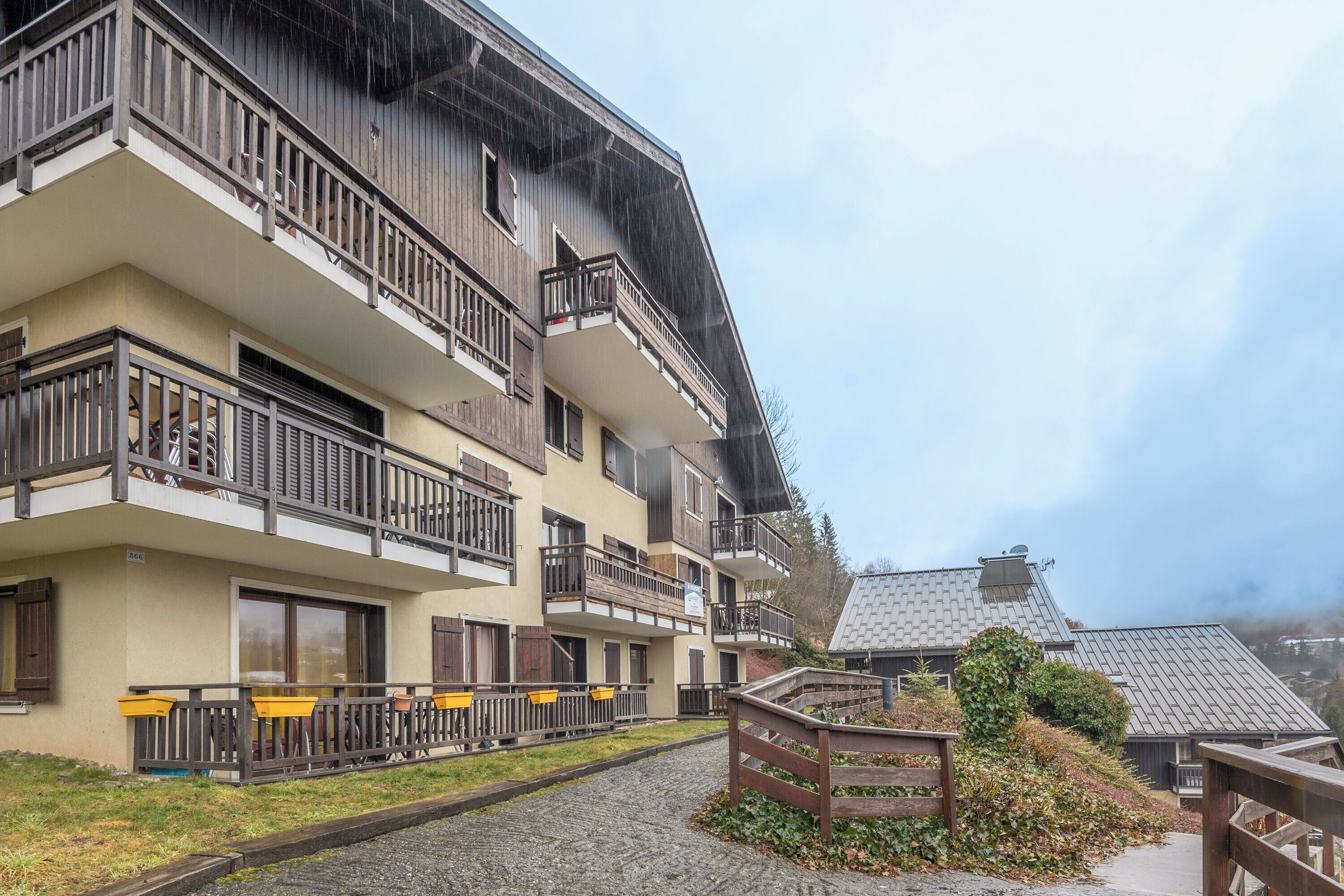 A multi-story building with balconies, a cobblestone pathway, and a wooden fence.