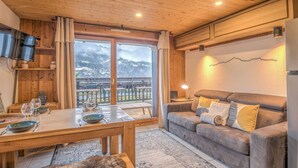 A wooden interior with a dining table, sofa, and a TV mounted on the wall. - Appartement Rocca - Welkeys (Saint-Gervais-les-Bains)