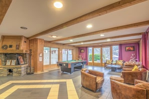 A spacious indoor area with a pool table, comfortable seating, and a stone fireplace. - Appartement Rocca - Welkeys (Saint-Gervais-les-Bains)