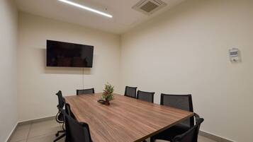 A conference room with a long table, black chairs, a small Christmas tree, a flat-screen TV, and a ceiling vent.
